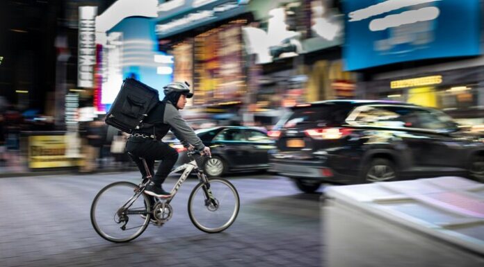 Maximize Earnings as a College Student with Food Delivery Apps Image of an individual writing to deliver while on a bicycle in NYC.